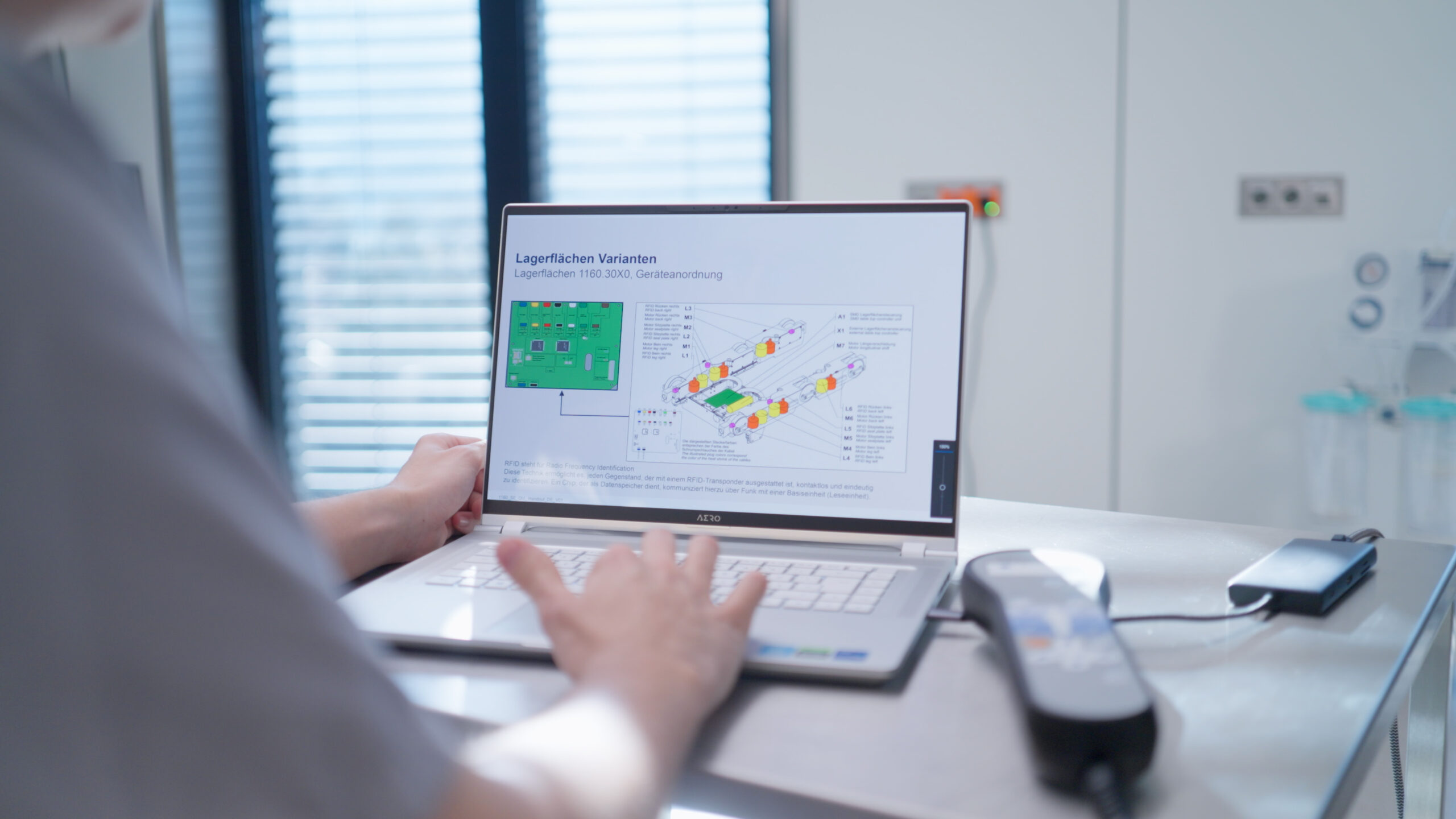 Person arbeitet am Laptop mit technischem Plan; Messgerät liegt daneben.